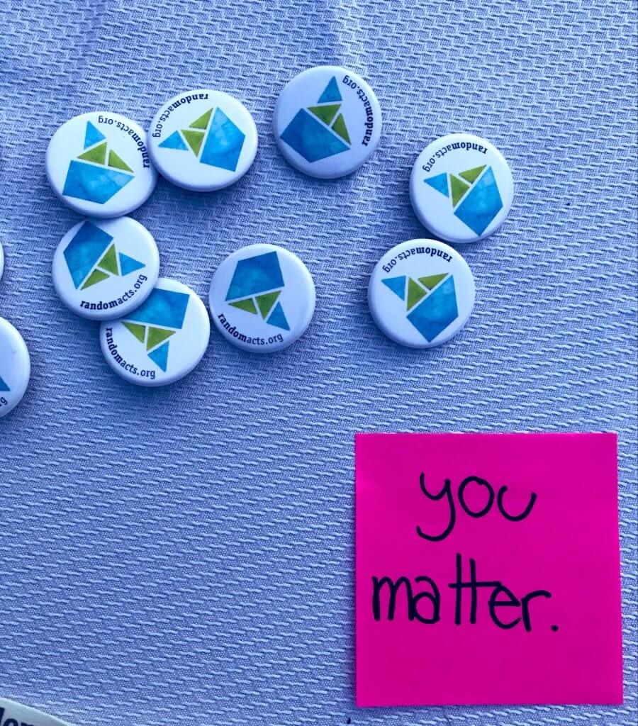 Random Acts buttons on a blue tablecloth next to a pink sticky note saying "you matter"
