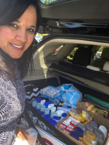 A woman smiling at the camera in front of a car trunk full of boxed hygiene items