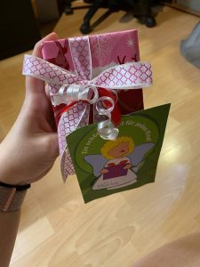 A hand holding a Christmas present in pink wrapping paper with a green card attached to it