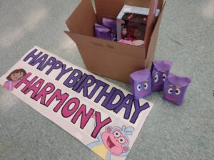 A Dora themed Birthday Box containing party bags and gifts for a chilrden's birthday party, and a sign reading 'Happy Birthday Harmony'