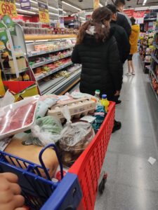 A shopping cart full of groceries behind a line of people