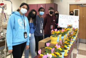 Students in masks stand in front of colorful potted plants