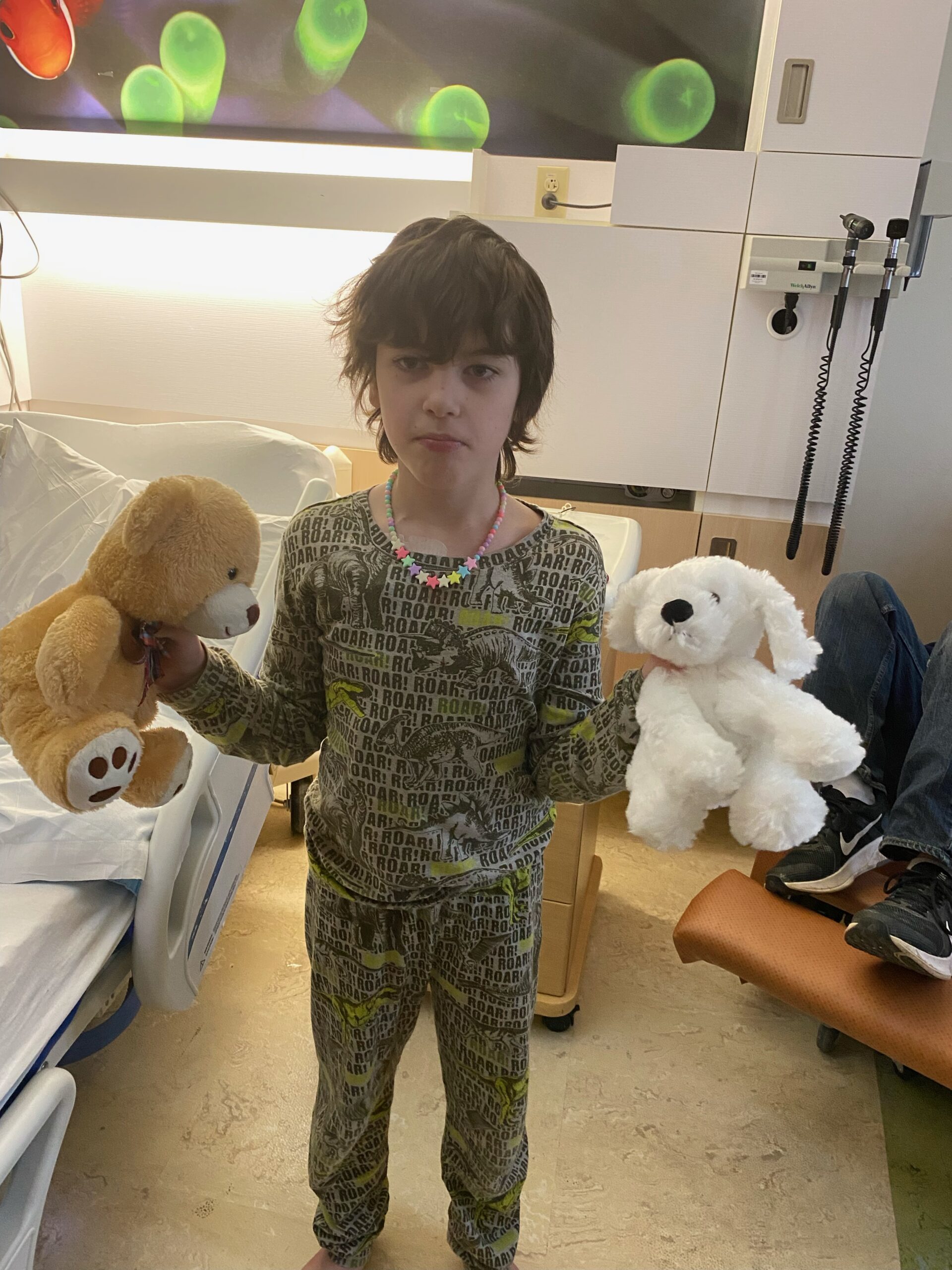 A child hospital patient holding 2 stuffed animals, 1 in each hand 
