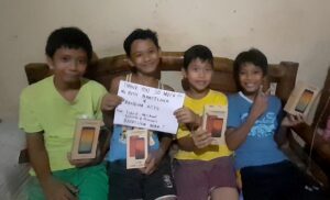 Four children in The Philippines sit with their new e-learning devices and hold a thank you sign