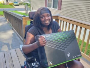 Dominique who lives with quadriplegia, sits in her mobility device holding her new Xbox