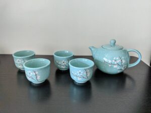 A light blue teapot and 4 light blue tea cups. The cups and the pot have a pattern with small white flowers.