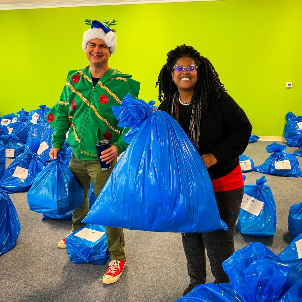 man and woman in holiday costumes holding blue Santa bag