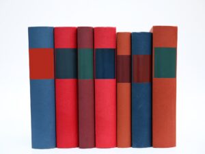 Image is of 7 generic books of different colors, with no title or author visible.