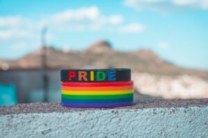 A black bracelet with the word "Pride" on it in rainbow colors, on top of a rainbow striped bracelet