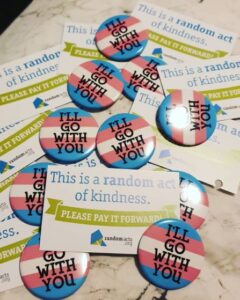 Transgender pride pins with the phrase "i'll go with you" and random acts spark cards on a white background