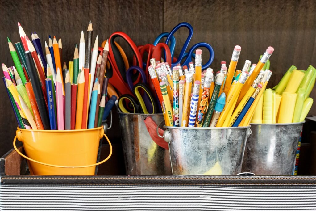 Small metal buckets sitting in a striped tray hold colored pencils, highlighters, and scissors.